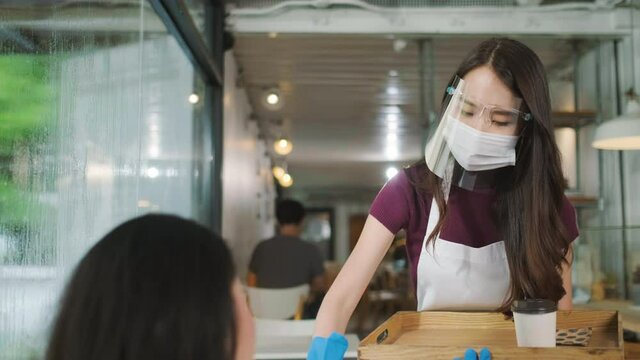 Asian waitress with face protective mask and face shield serving coffee and bread in coffee shop