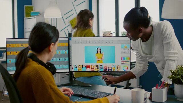 Diverse photo editors sitting in creative workplace retouching photos, african director checking color greding technic talking with worker. Retouchers editing with graphic tablet and stylus pencil