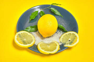 whole lemon and chopped lobules on blue plate with sugar and green leaves