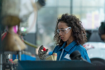 A female car mechanic holding a bottle of brake fluid and engine oil to be exchanged for a customer. Auto mechanic female automotive diagnostic Checking car service, repair, maintenance.