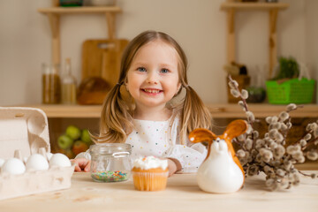 Cute little girl in a cotton dress at home in a wooden kitchen prepares an Easter cake
