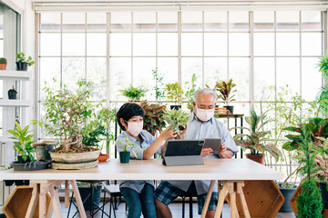 Asian retirement grandfather and grandson wearing a face mask and live to sell plants on a tablet...