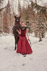 Obraz premium A girl in a vintage red dress stands next to a horse in a winter forest.