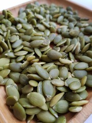 Green pumpkin seeds lie on a wooden plate