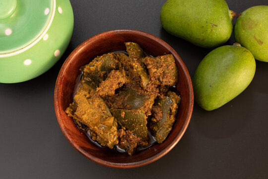 Mango pickle or Traditional spicy Indian mango pickle with ceramaic jar and raw mango, selective focus isolated on black