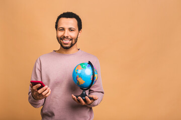 Cheerful african american black man holding the globe with love and care isolated over beige background. Travel concept, looking for a jorney. Using mobile phone.