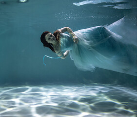 beautiful girl with red hair in a ball gown blue dress underwater on a blue background