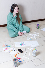 White teenage girl sitting on the floor in headphones, drawing, looking away.