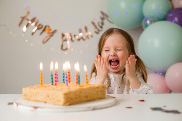 cute little girl blows out candles on a birthday cake at home against a backdrop of balloons. Child's birthday - Powered by Adobe