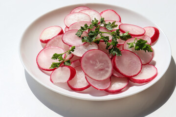 Fresh radish salad with parsley on white background. Top view, copy space. Spring summer vegetable salad on white plate