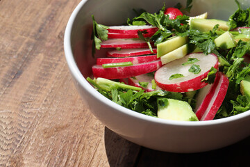 Salad with avocado and radish in white bowl on rustic wooden background. Top view