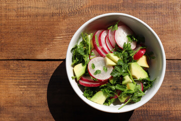 Salad with avocado and radish in white bowl on rustic wooden background. Top view