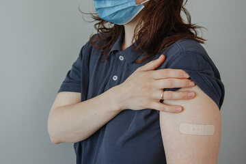 Portrait of a young woman shows arm with patch, after having the vaccine against Coronavirus Covid-19 immunizing. Person bares shoulder after injection