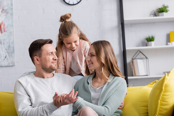 Smiling papers holding hands near daughter at home.