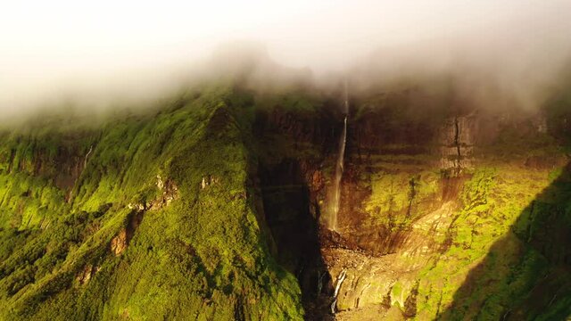 Drone flying between green mountains of Poco Ribeira do Ferreiro, Alagoinha, Flores Island, Azores, Portugal, Europe. Picturesque landscape with waterfall and clouds, 4k footage