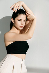 beautiful brunette in trousers and a short top leaning against the white wall