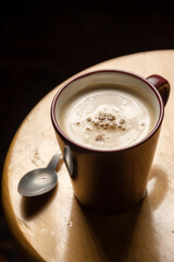 Aerial view of cup of cappuccino coffee and spoon on wooden stool, on black background, in vertical, with copy space