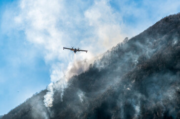 Fototapeta na wymiar Firefighting Aircraft dropping the water for fighting a fire on mountain above Lake Ghirla in Valganna, province of Varese, Italy