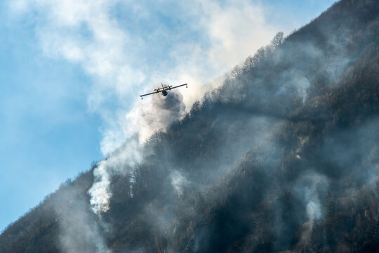 Firefighting Aircraft dropping the water for fighting a fire on mountain above Lake Ghirla in Valganna, province of Varese, Italy