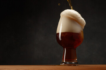 Glass of Beer on Dark Gray Background. Dark Ale Beer With Overflowing Foam Head. Stream of Stout Beer Pours Into a Beer Glass on a Bar Counter.