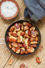 Vicia faba. Crispy fried (roasted) broad beans with salt in a frying pan close-up on a wooden old table.  Selective focus