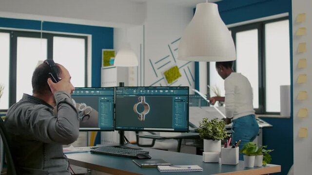 Mecanic technician working on cad software using computer with two monitors innovating an efficient eco-friendly motor prototype. Industrial man engineer studying new idea in creative office