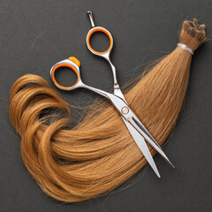 The cut strand of childrens female hair is light brown on a dark background, top view, hairdressing services