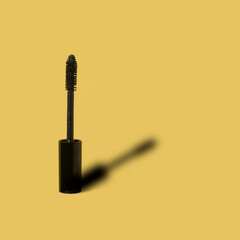 Black mascara with shadow on yellow background. Minimal make up, beauty or cosmetic concept.