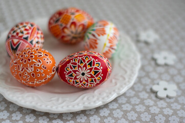 Homemade handmade painted Easter eggs on white plate dish on tablecloth with white petal flowers, Eastertime decoration