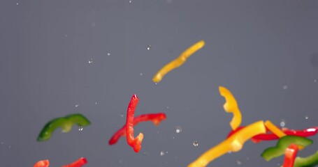 SUPER SLOW MOTION Red green yellow cut pepper slices flying along with water drops against bright background. Shot with high speed camera, 420 FPS