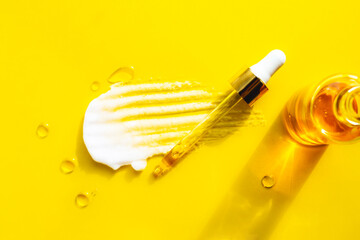 White smear of foam on yellow background. Oil drops, glass bottle with serum, pipette. Trendy beauty product wellness banner