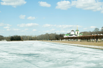 Panoramic views of the church spire and the ice-covered park pond. April 10, 2021, Kuskovo, Moscow, Russia.