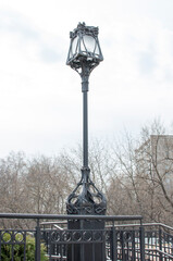 Close-up of lighting of a lamppost against the backdrop of city houses against a blurred background.