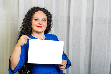Curly joyful brunette woman on a chair holds a copy space plate in her hands.