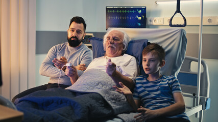 Aged man celebrating victory of favorite team with son and grandson in hospital ward