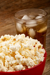 Bowl with salted popcorn and soda on the table.