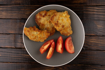 Meat in batter in a gray plate with slices of tomatoes