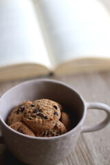 Bowl of chocolate chip cookies and open book on a table. Selective focus.