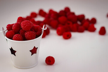 Red ripe and juicy raspberry in a small white bucket with stars