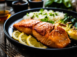 Fried salmon steak with lemon, jasmine rice and fried pak choi cabbage served on wooden table
