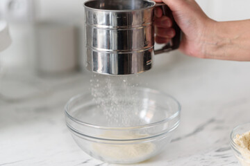 Close-up of a woman's hands sifting flour through a flour sifter.