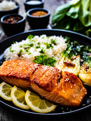 Fried salmon steak with lemon, jasmine rice and fried pak choi cabbage served on wooden table
