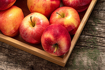Ripe garden apple fruits in basket in wooden tray on wooden table