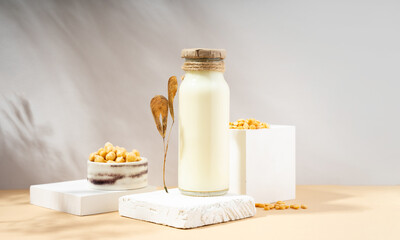 Vegetable pea milk in a bottle and chick peas in handmade ceramic bowl on white podium, pedestal on beige background. shadows. dry leaves. Gluten-free, lactose-free vegan product. Modern. Copy space