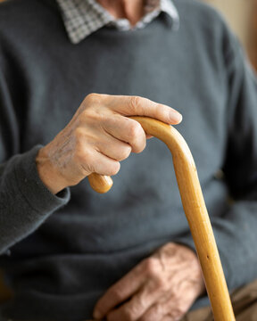 Old man's hands holding wooden walking stick