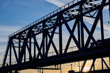 The silhouette of the metal structure of the railway bridge at sunset. Engineering structure made of steel against the sky.
