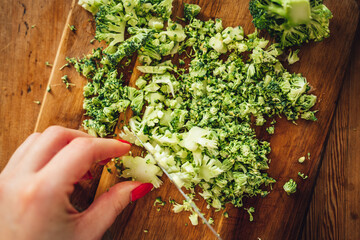 Closeup of a female chopping the fresh and tasty broccoli with a knife on a wooden cutting board