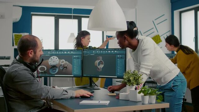 Multiethnic team discussing about industrial project using dual monitors setup to desing 3D metalic pieces in CAD software. Industrial engineer and african manager working together in creative office