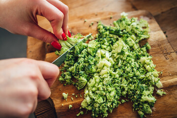 Closeup of a female chopping the fresh and tasty broccoli with a knife on a wooden cutting board