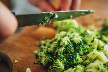 Closeup of a female chopping the fresh and tasty broccoli with a knife on a wooden cutting board
